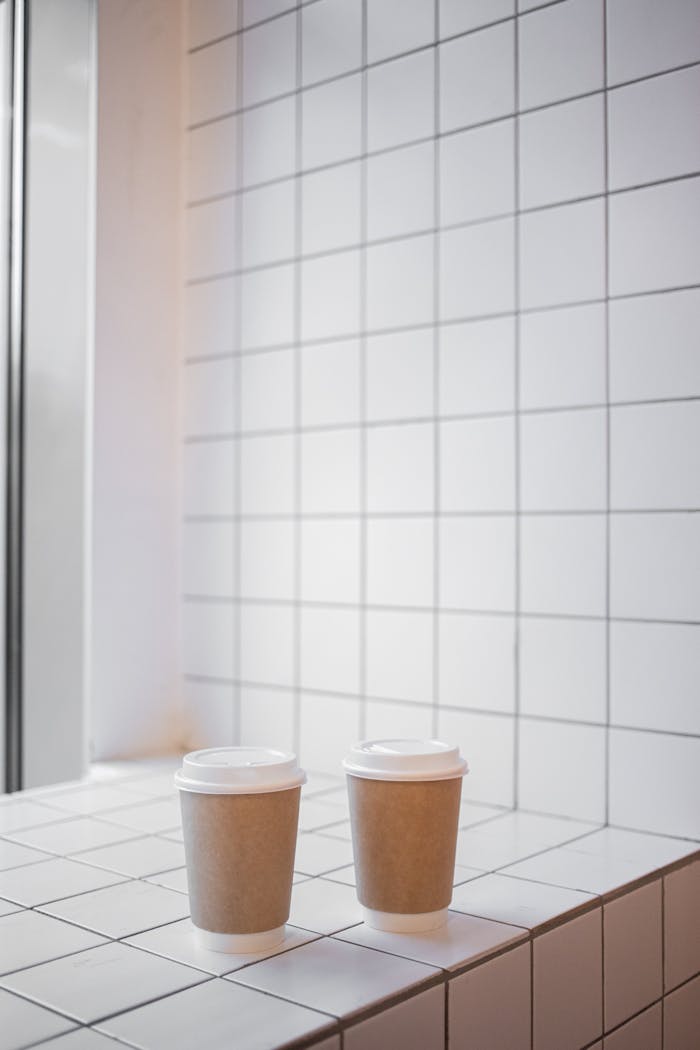 Two paper coffee cups on a white tiled surface with copy space, perfect for café ambiance.